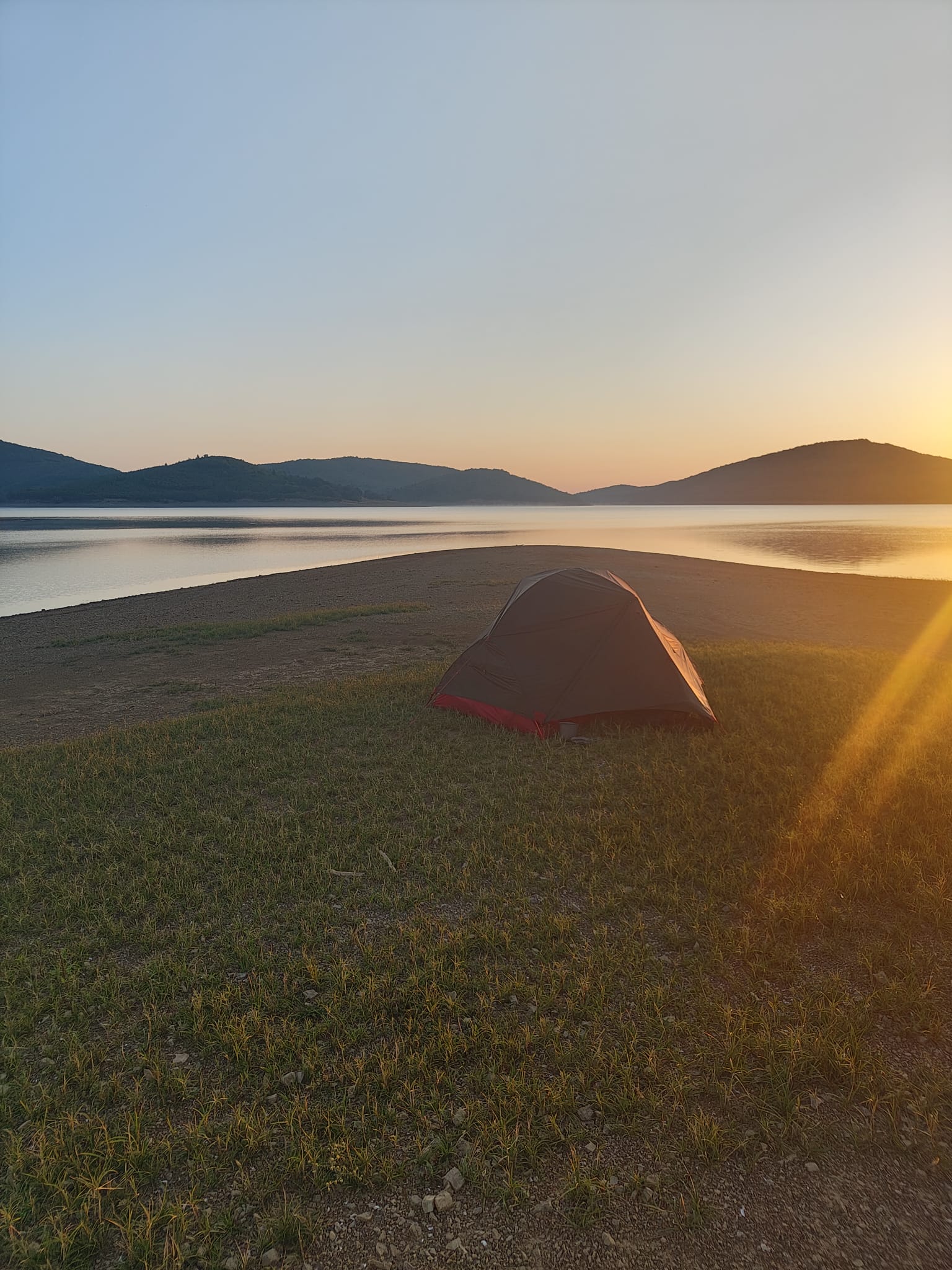 Une tente montée sur la rive d’un lac, avec les montagnes à l’arrière-plan.