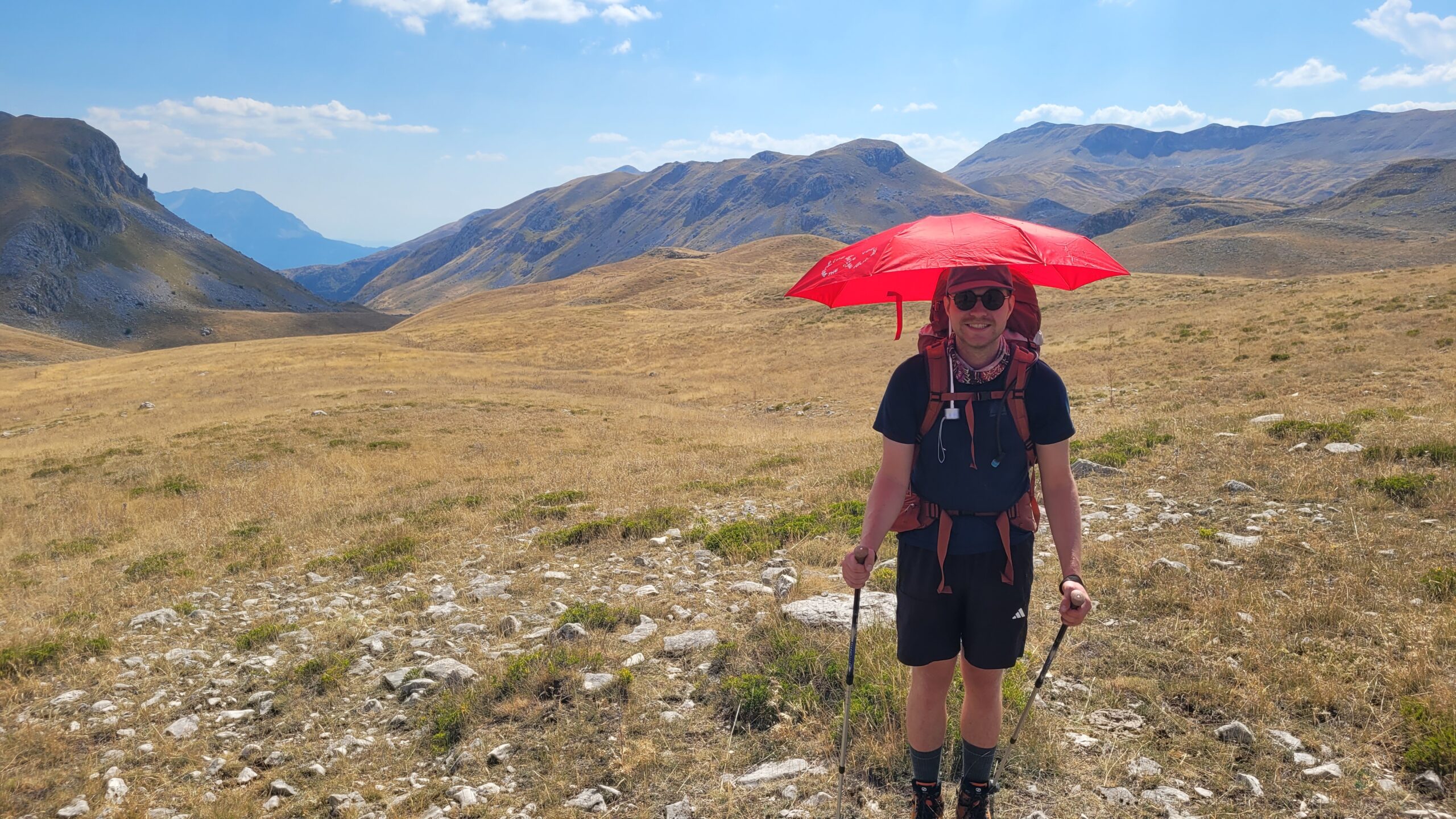 Un scout cherche de l’ombre sous un parapluie ouvert.