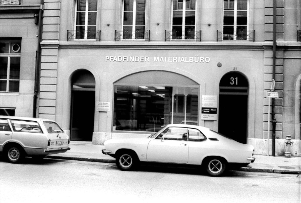 Frontansicht des Pfadimaterialbüros in Bern als Schwarz-Weiss-Foto. Vor dem Haupteingang sind zwei Fahrzeuge parkiert.